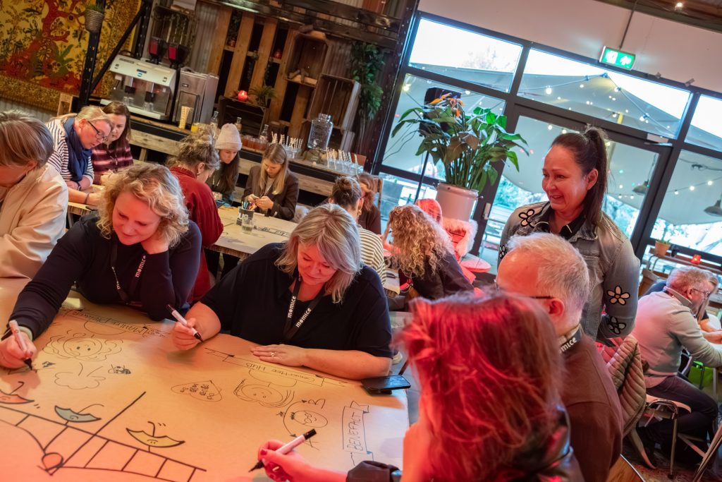Deelnemers tekenen samen aan een grote illustratietafel tijdens een live illustratie workshop en interactieve event activatie van Studio Limón.